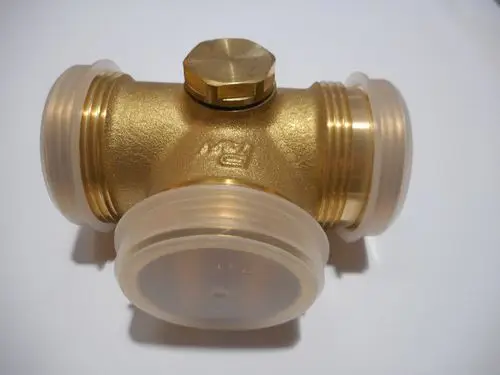 T-Stück aus Messing mit zwei transparenten Kunststoffanschlüssen und einem Deckel. Produkt von Remeha, geeignet für Rohrverbindungen in Heizungs- oder Sanitärinstallationen.